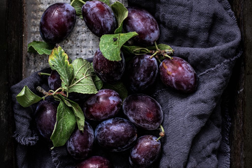 A photograph of freshly picked plums on top of a blanket. They look delicious and ready to bake into a crumble. 