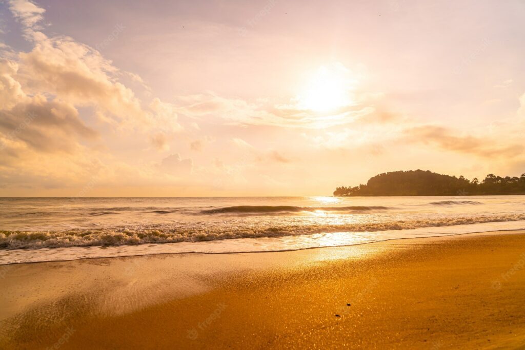 A cosy sunset over Gylly beach. Sat on the sand the picture shows the small waves making their way over deep orange sand. The sun is in the sky and glows orange and purple.